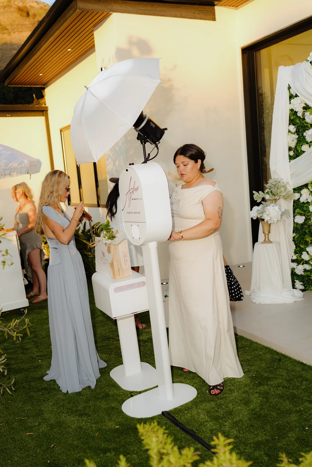 An Ageless Moments LA photo booth set up beside a floral arch at an outdoor Los Angeles celebration