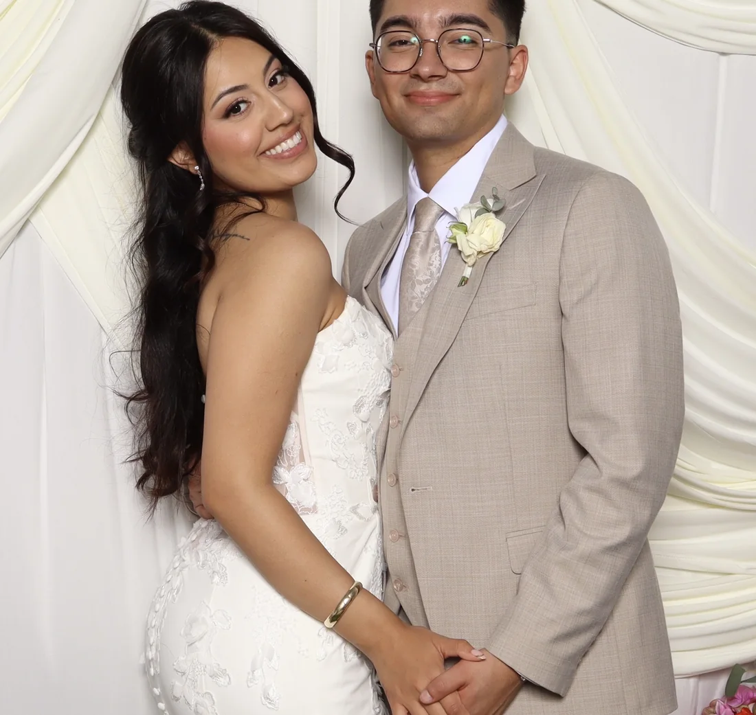 A couple posing in front of ivory pleated drapery at the photo booth