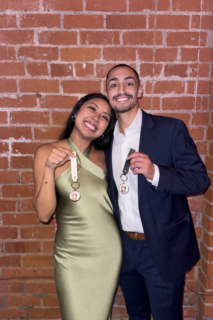 Couple against a red brick wall holding up keychains with round photo charms