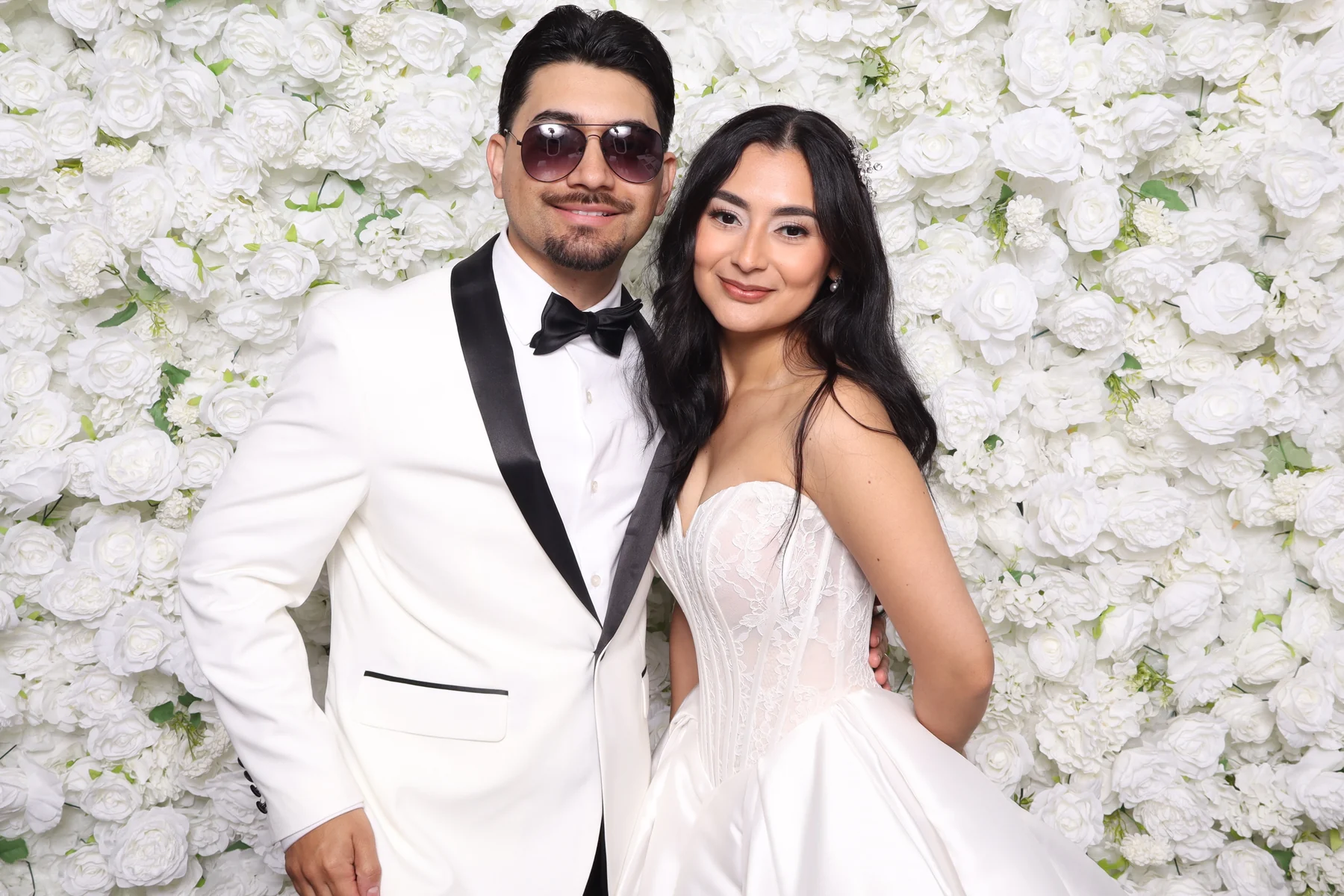 A couple photographed at the wedding photo booth in front of a white flower wall in Los Angeles