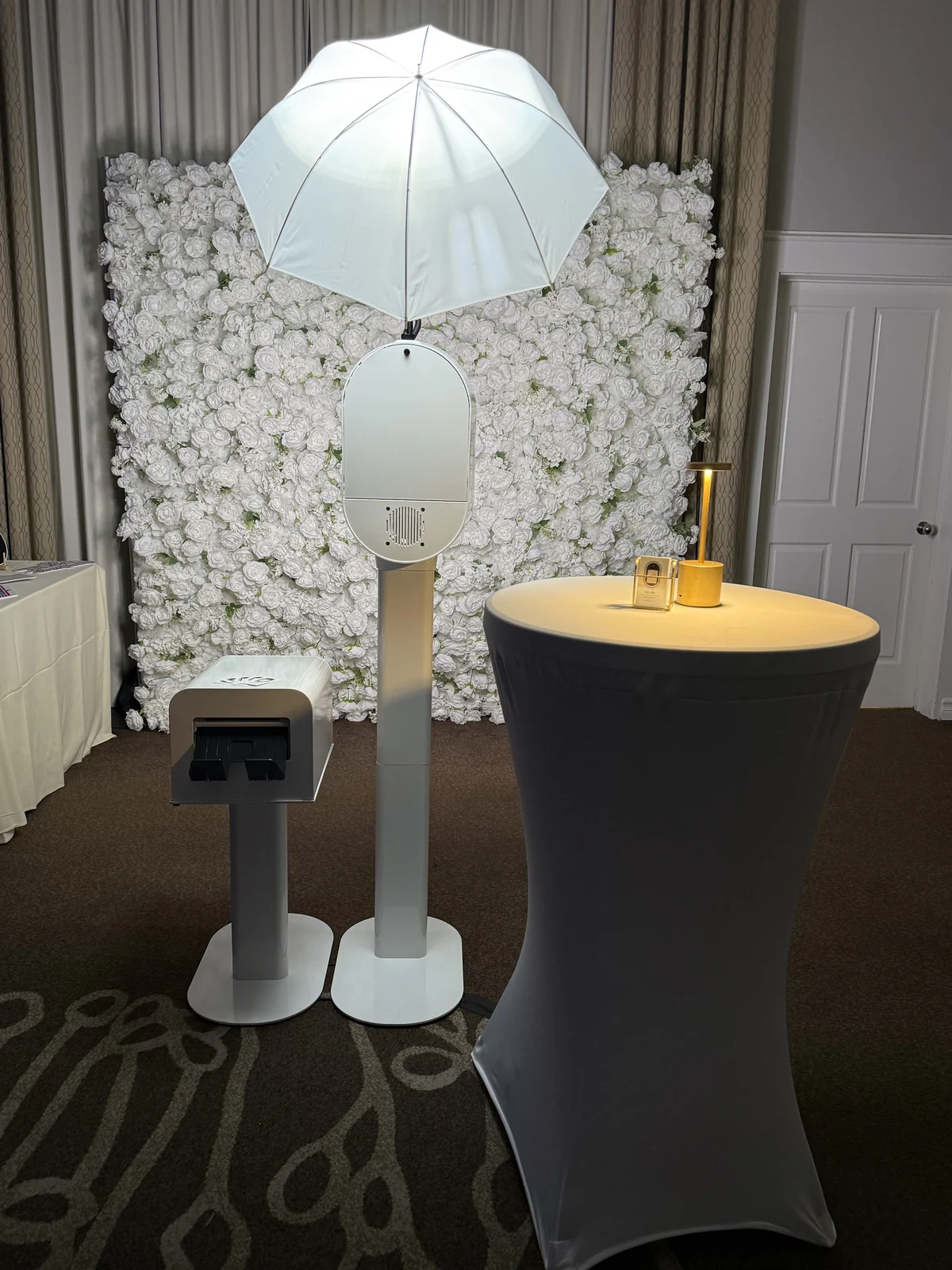 An Ageless Moments LA photo booth set up with its print dispenser beside a white flower wall