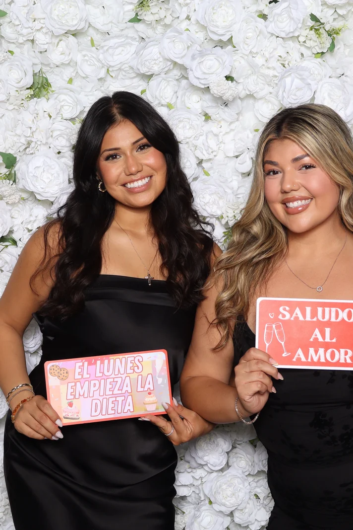 Two guests posing in front of the white flower wall backdrop