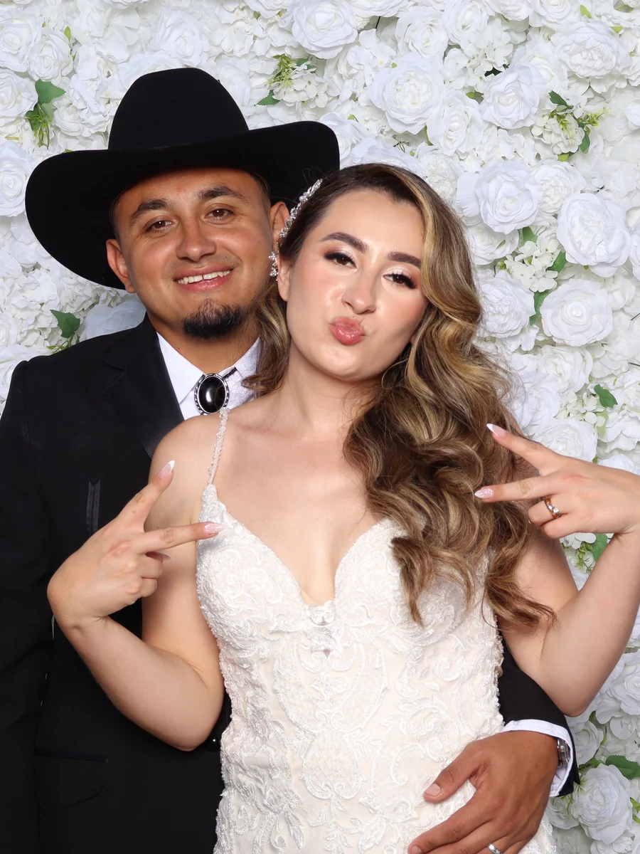 A couple at the photo booth in front of a white flower wall