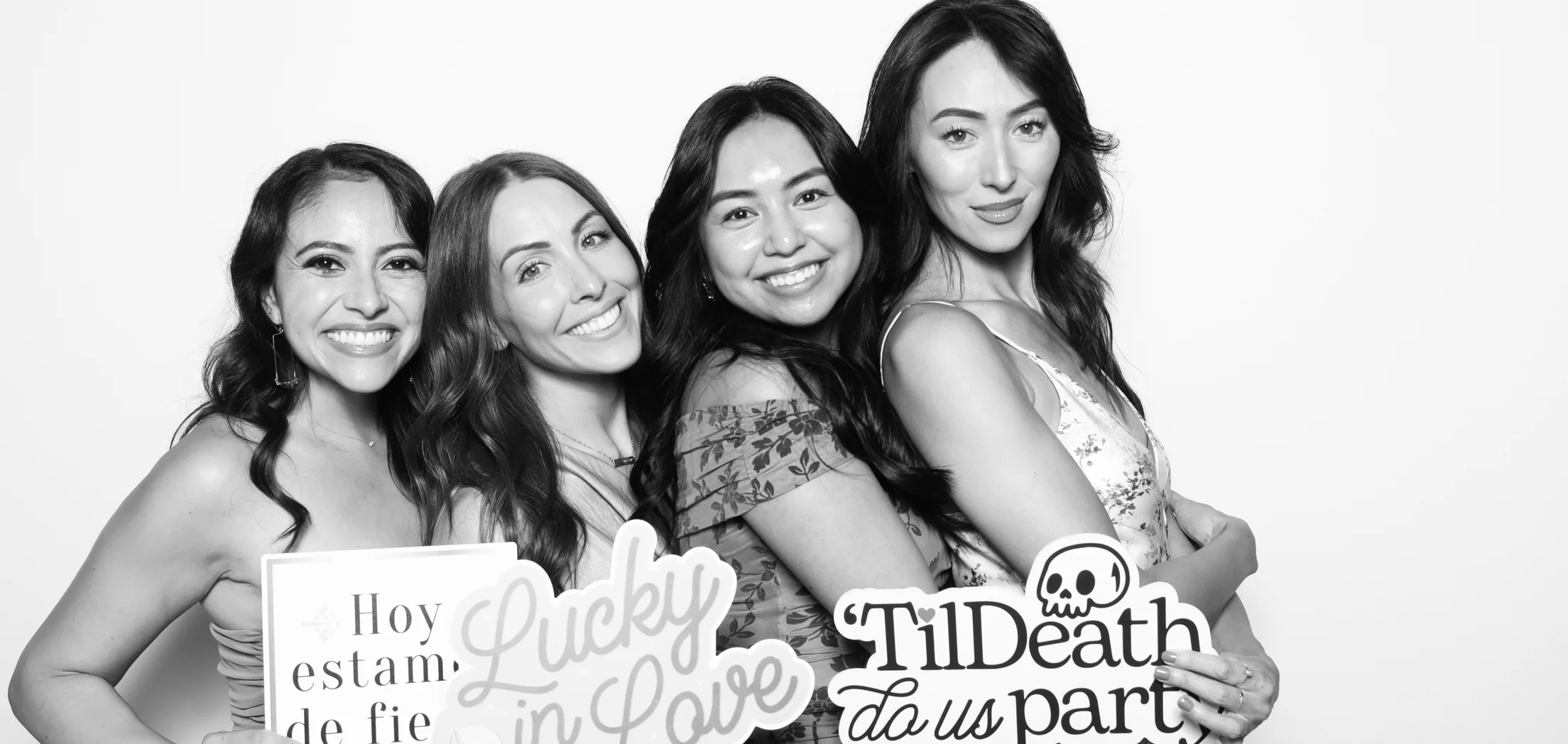 Four guests posing together with props in a black and white booth photo