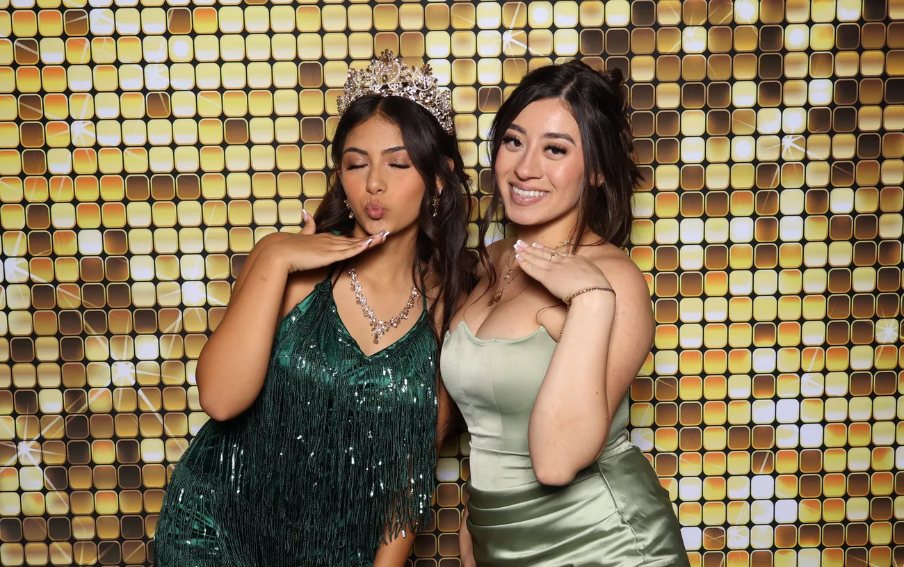 Two guests in front of the gold sequin backdrop at a quinceañera