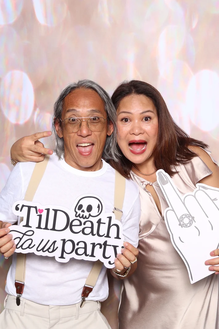 Two guests laughing with props in front of the flower wall backdrop