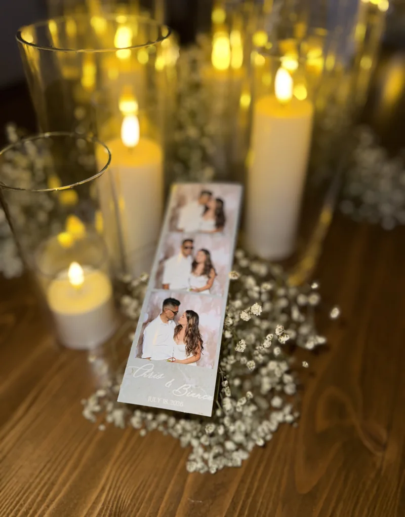 A printed photo strip propped among candles and baby's breath on a wooden table