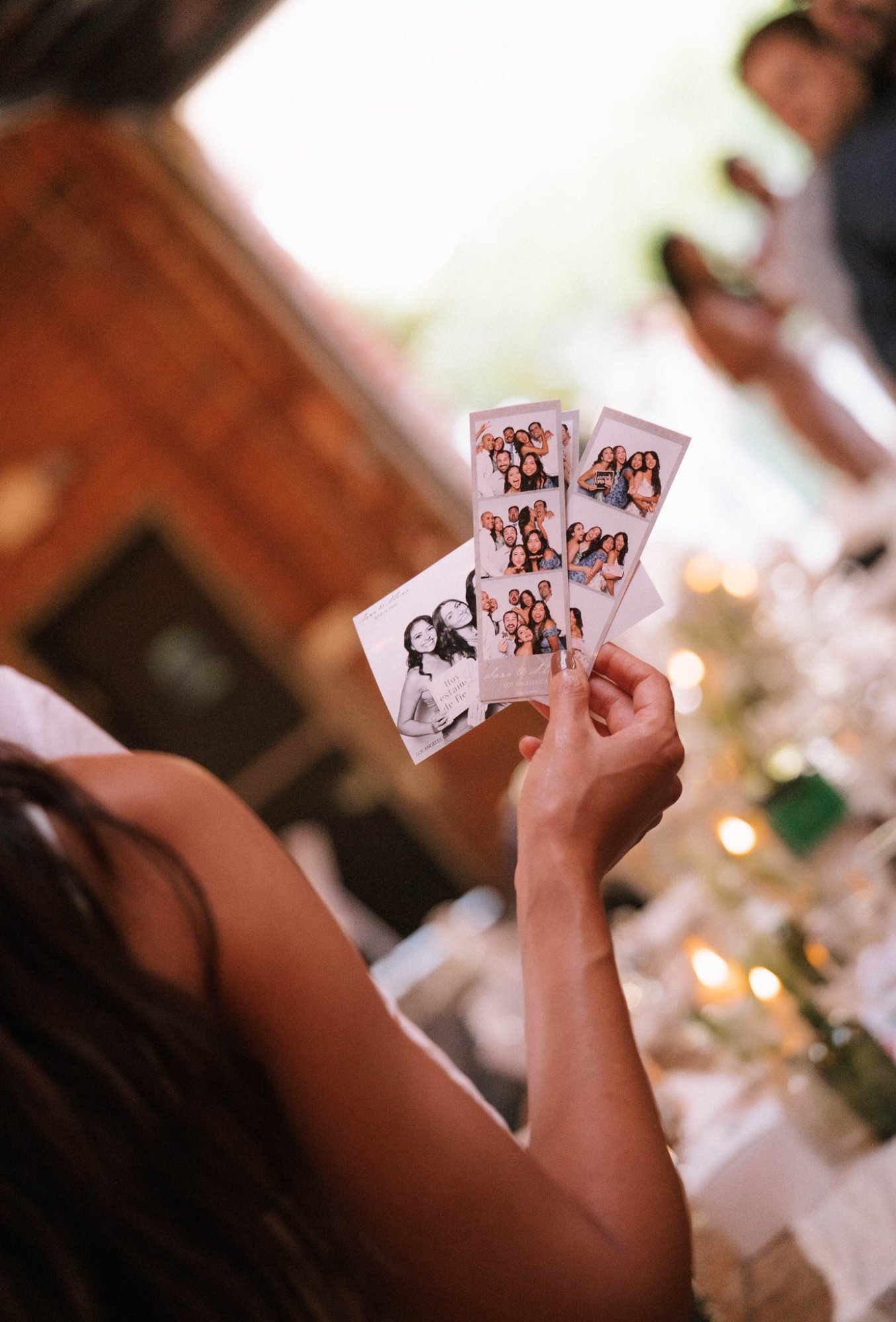 A guest holds up a fan of photo booth strips above a candlelit reception table